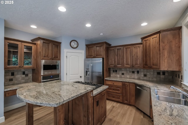 kitchen with sink, a breakfast bar, stainless steel appliances, light stone counters, and light hardwood / wood-style floors