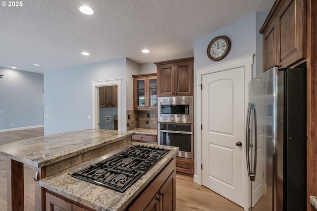 kitchen featuring a kitchen bar, appliances with stainless steel finishes, a kitchen island, light stone countertops, and light hardwood / wood-style floors