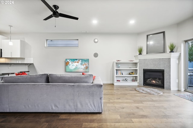 living room featuring ceiling fan, a tiled fireplace, and light wood-type flooring