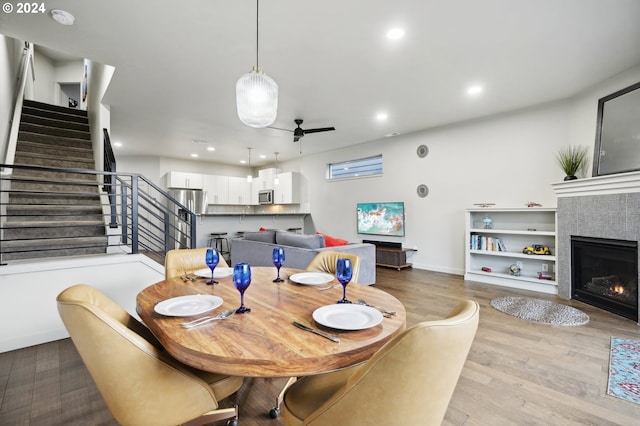 dining area with a tile fireplace, light hardwood / wood-style floors, and ceiling fan