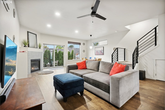 living room featuring ceiling fan, a tile fireplace, and light hardwood / wood-style flooring