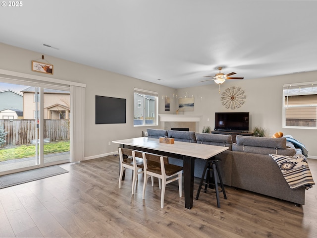 dining area with a tile fireplace, wood-type flooring, and ceiling fan