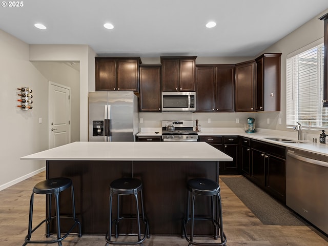 kitchen with sink, a breakfast bar, stainless steel appliances, a center island, and wood-type flooring