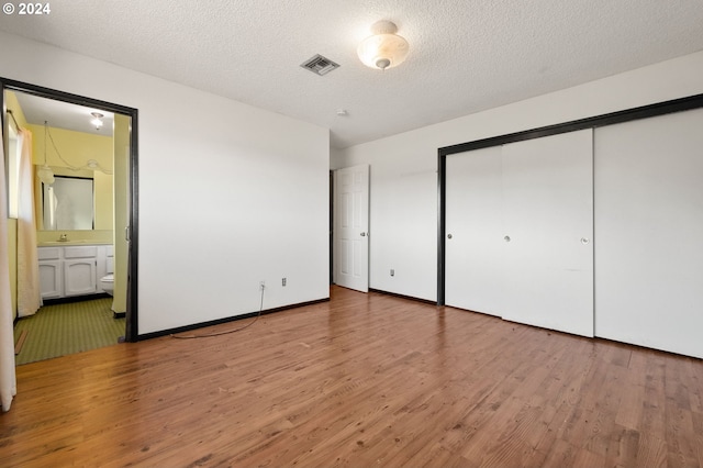 unfurnished bedroom with a closet, a textured ceiling, connected bathroom, and hardwood / wood-style floors