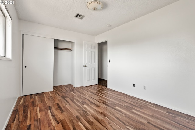 unfurnished bedroom with a textured ceiling, a closet, and dark hardwood / wood-style floors