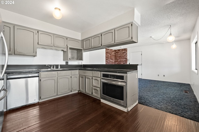 kitchen with appliances with stainless steel finishes, gray cabinetry, dark wood-type flooring, a textured ceiling, and sink