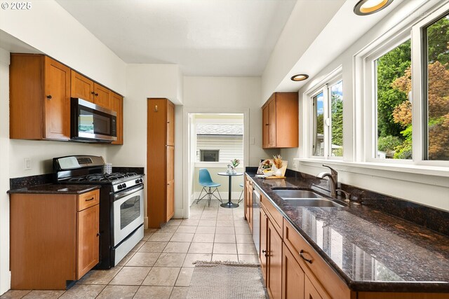 5125 NE Davis St, Portland, OR 97213 - kitchen with appliances with stainless steel finishes, a sink, brown cabinetry, light tile patterned floors, and dark stone counters
