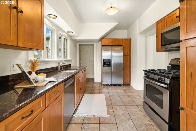 5125 NE Davis St, Portland, OR 97213 - kitchen featuring appliances with stainless steel finishes, a sink, brown cabinetry, dark stone counters, and baseboards