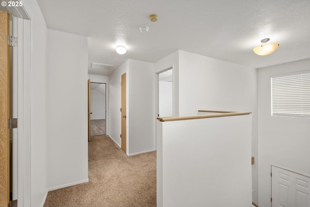 hallway with an upstairs landing, light colored carpet, a textured ceiling, and baseboards