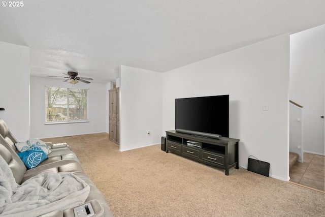 carpeted living area with a textured ceiling, stairs, and ceiling fan