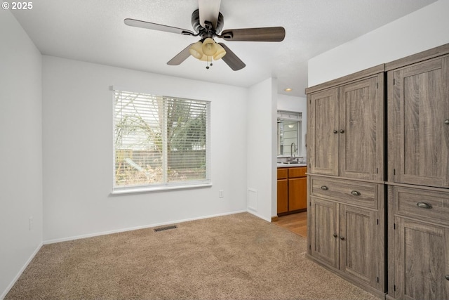 unfurnished bedroom with visible vents, baseboards, light colored carpet, ensuite bathroom, and a sink