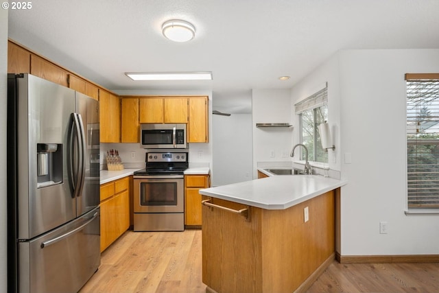 kitchen featuring a peninsula, a sink, stainless steel appliances, light countertops, and light wood-type flooring