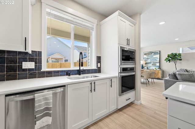 kitchen featuring a sink, light wood-style flooring, stainless steel appliances, open floor plan, and tasteful backsplash