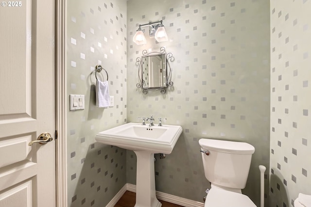 bathroom with a sink, toilet, and wallpapered walls