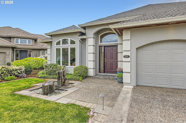 view of exterior entry featuring driveway, a yard, an attached garage, a shingled roof, and stucco siding