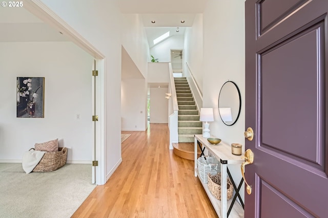 entryway with light wood-type flooring, baseboards, a skylight, and stairway