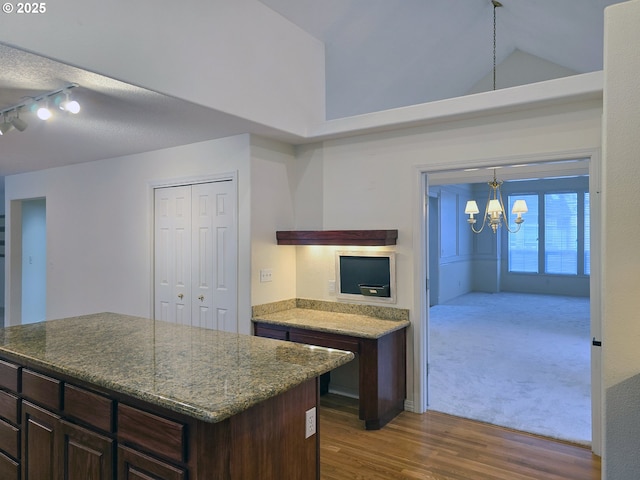 kitchen featuring pendant lighting, an inviting chandelier, a kitchen island, vaulted ceiling, and dark stone counters