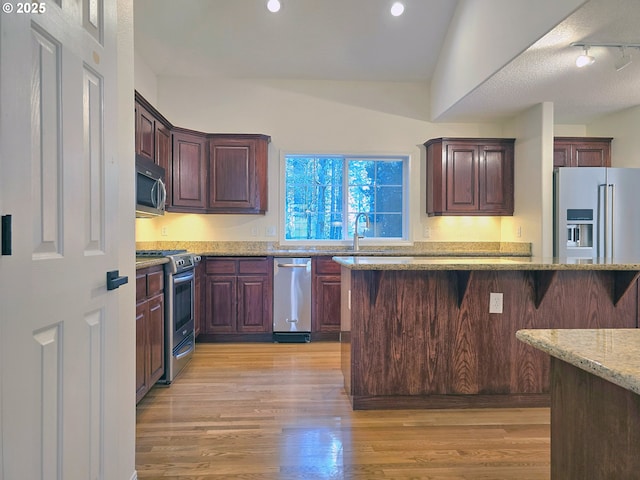 kitchen with a breakfast bar, sink, light hardwood / wood-style floors, stainless steel appliances, and light stone countertops