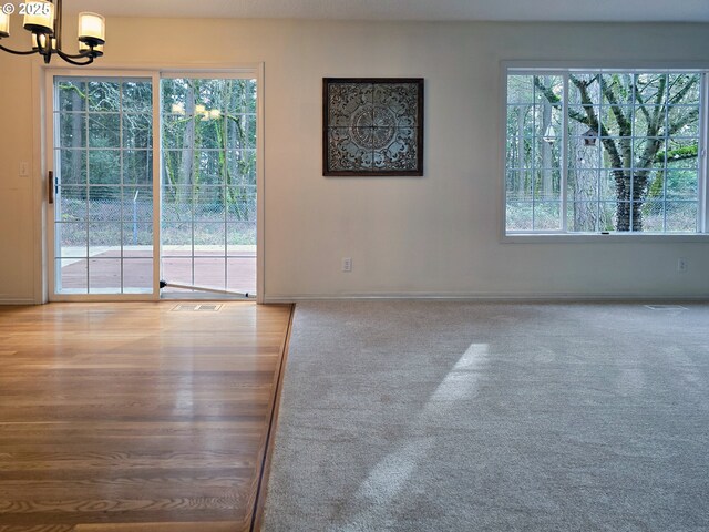 carpeted empty room featuring a notable chandelier and a healthy amount of sunlight