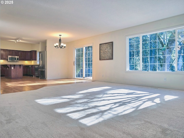 unfurnished living room featuring a healthy amount of sunlight, light colored carpet, and an inviting chandelier