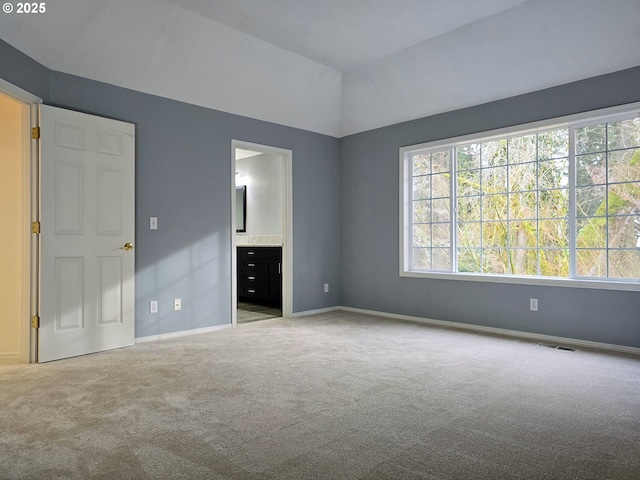 unfurnished bedroom featuring light colored carpet, lofted ceiling, and ensuite bath