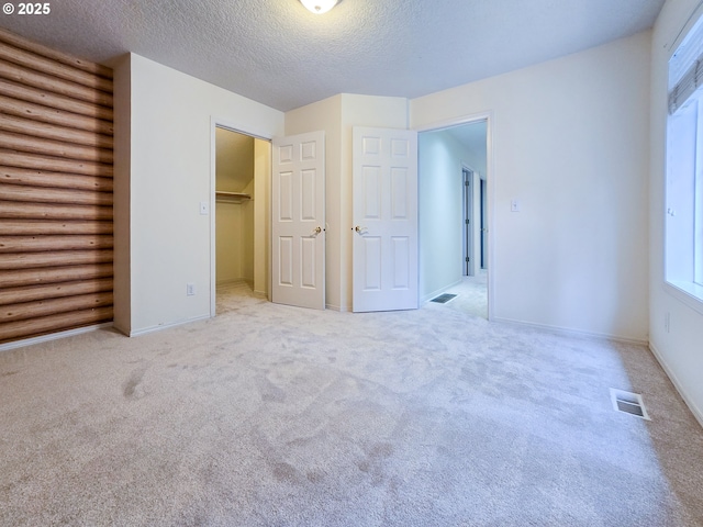 unfurnished bedroom with light colored carpet, a spacious closet, rustic walls, and a textured ceiling