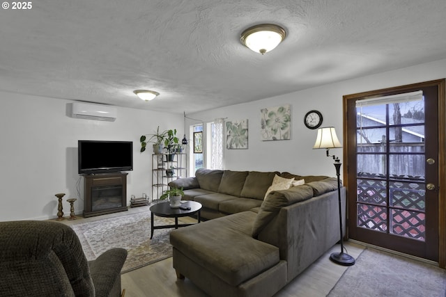 living area featuring a glass covered fireplace, a textured ceiling, and a wall mounted air conditioner