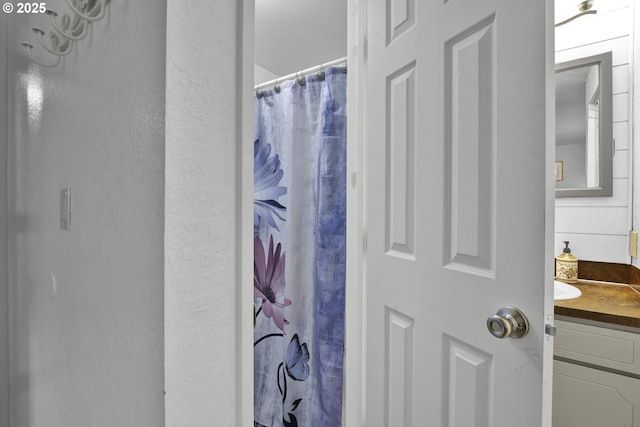 bathroom with vanity, curtained shower, and a textured wall