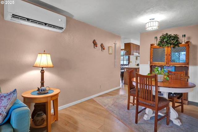 dining area featuring an AC wall unit, baseboards, and light wood-type flooring