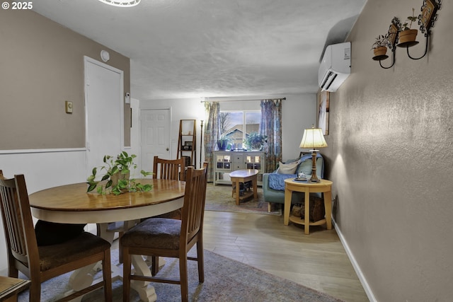 dining room featuring a wall mounted air conditioner, baseboards, wood finished floors, and a textured wall