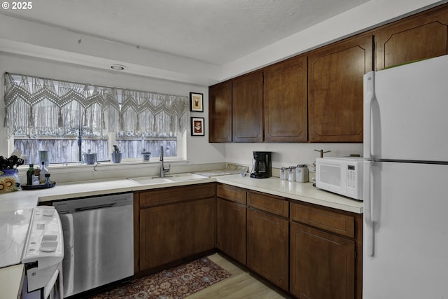 kitchen featuring light wood-style flooring, a sink, a textured ceiling, white appliances, and light countertops