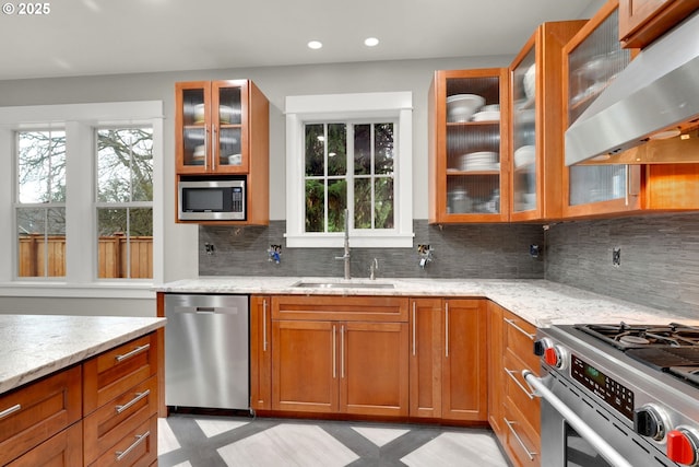 kitchen featuring brown cabinets, a sink, light stone counters, appliances with stainless steel finishes, and extractor fan