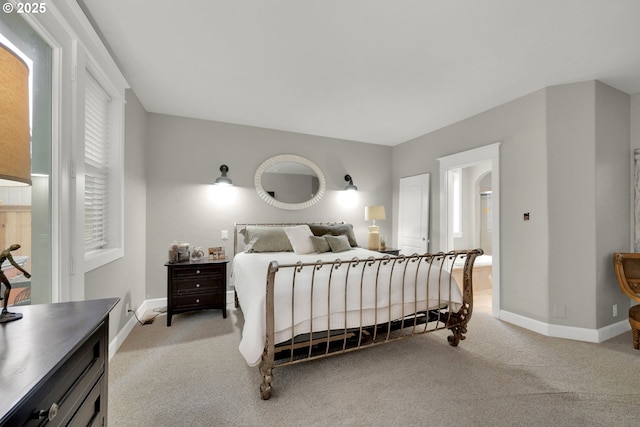 bedroom with baseboards, ensuite bathroom, and light carpet