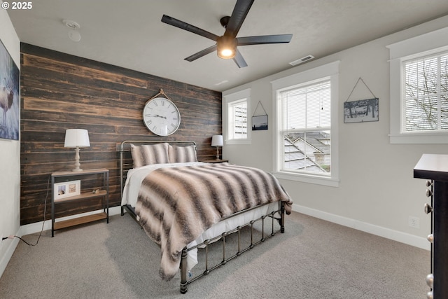 carpeted bedroom with an accent wall, wooden walls, multiple windows, and visible vents