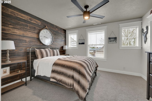 carpeted bedroom featuring visible vents, wooden walls, an accent wall, baseboards, and a ceiling fan