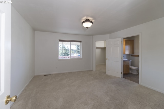 1985 32nd St, Florence, OR 97439 - unfurnished bedroom featuring ensuite bath, baseboards, a walk in closet, and light colored carpet
