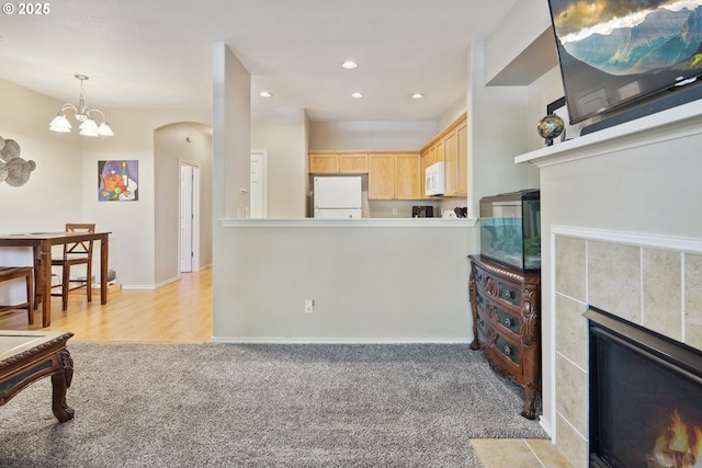 carpeted living room featuring a tiled fireplace and a notable chandelier