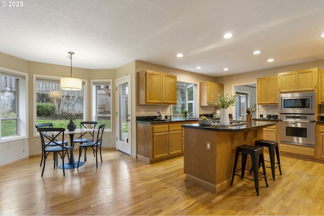 kitchen with dark countertops, a kitchen island, a kitchen bar, light wood-style flooring, and appliances with stainless steel finishes