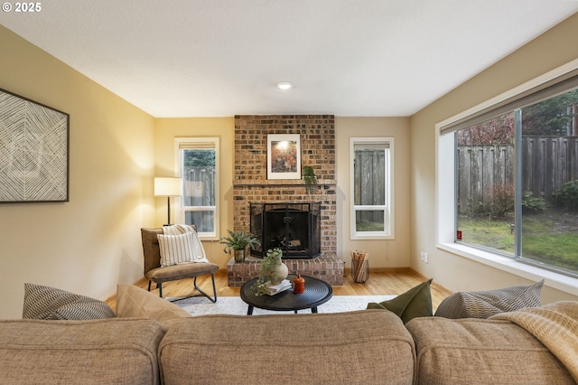 living area with baseboards, a brick fireplace, a healthy amount of sunlight, and wood finished floors