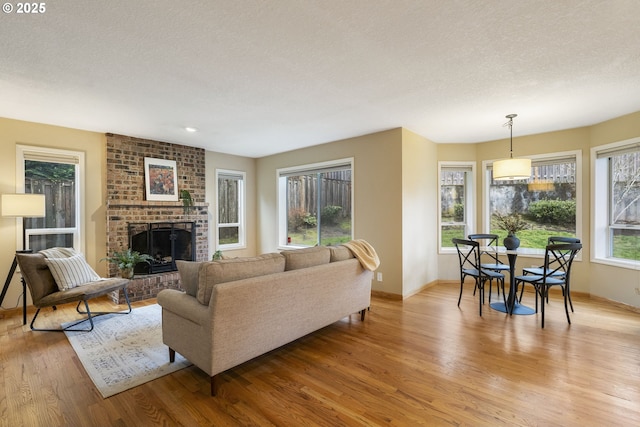 living room featuring light wood finished floors, a brick fireplace, a textured ceiling, and baseboards