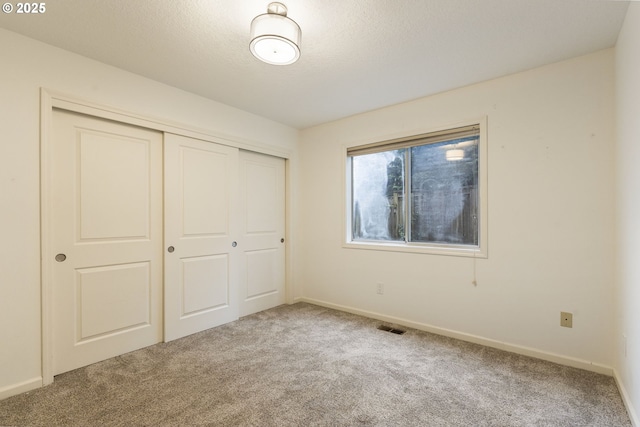 unfurnished bedroom with visible vents, a textured ceiling, a closet, carpet flooring, and baseboards