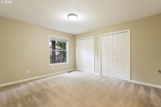 unfurnished bedroom with baseboards, multiple closets, a textured ceiling, and carpet floors