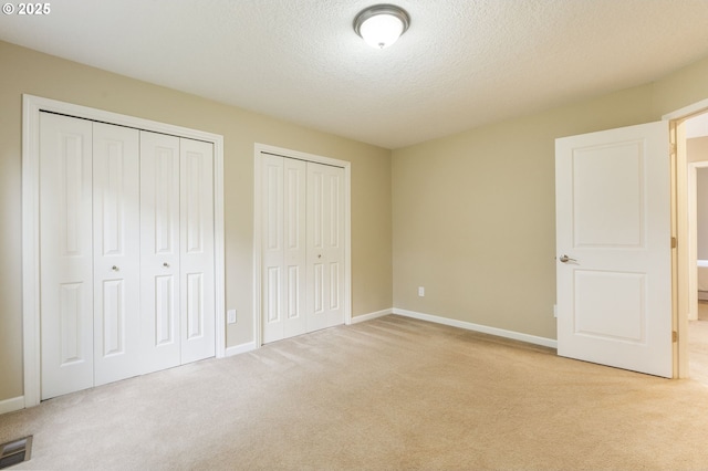 unfurnished bedroom featuring visible vents, baseboards, multiple closets, carpet floors, and a textured ceiling