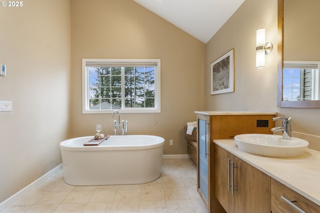 bathroom with a freestanding bath, vanity, baseboards, and vaulted ceiling