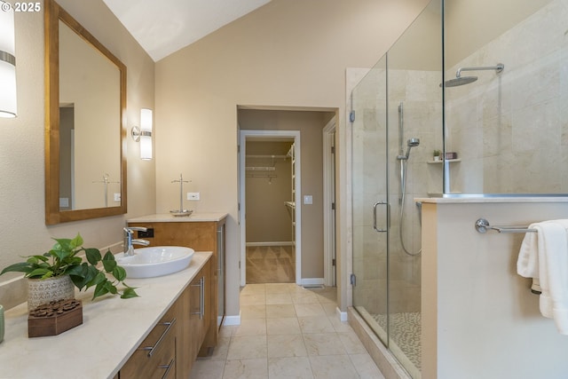 bathroom featuring a walk in closet, a stall shower, baseboards, lofted ceiling, and vanity