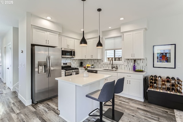 kitchen featuring a kitchen island, appliances with stainless steel finishes, decorative light fixtures, white cabinetry, and sink