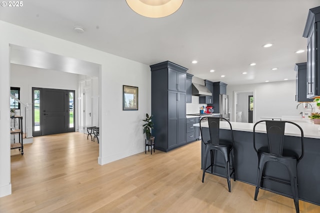 kitchen with a peninsula, wall chimney exhaust hood, high quality fridge, light wood-style flooring, and light countertops