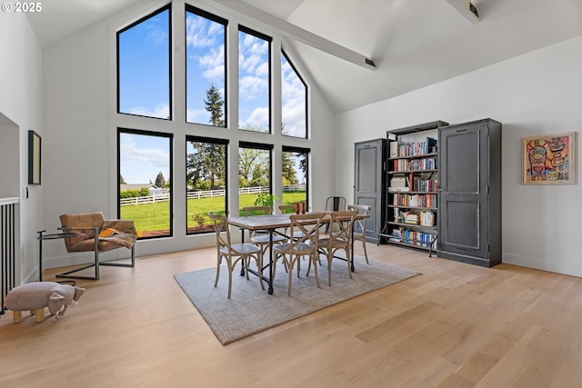 dining space featuring high vaulted ceiling, light wood-type flooring, baseboards, and beam ceiling