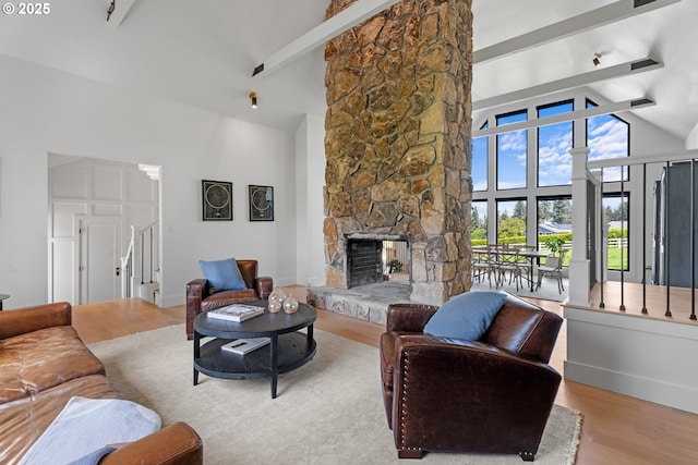 living room featuring beam ceiling, wood finished floors, high vaulted ceiling, and a stone fireplace