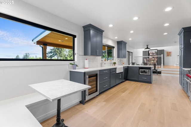 kitchen with beverage cooler, a peninsula, built in microwave, light countertops, and light wood-type flooring